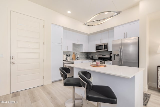 kitchen with light wood-type flooring, a center island, white cabinets, a breakfast bar area, and appliances with stainless steel finishes