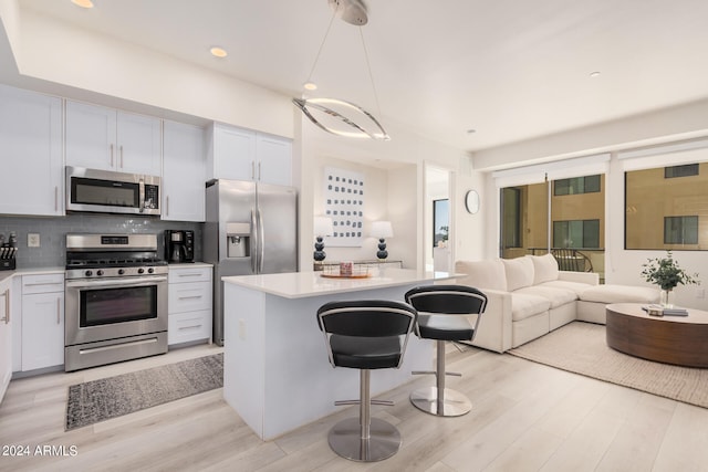 kitchen with white cabinets, hanging light fixtures, stainless steel appliances, a center island, and a kitchen bar