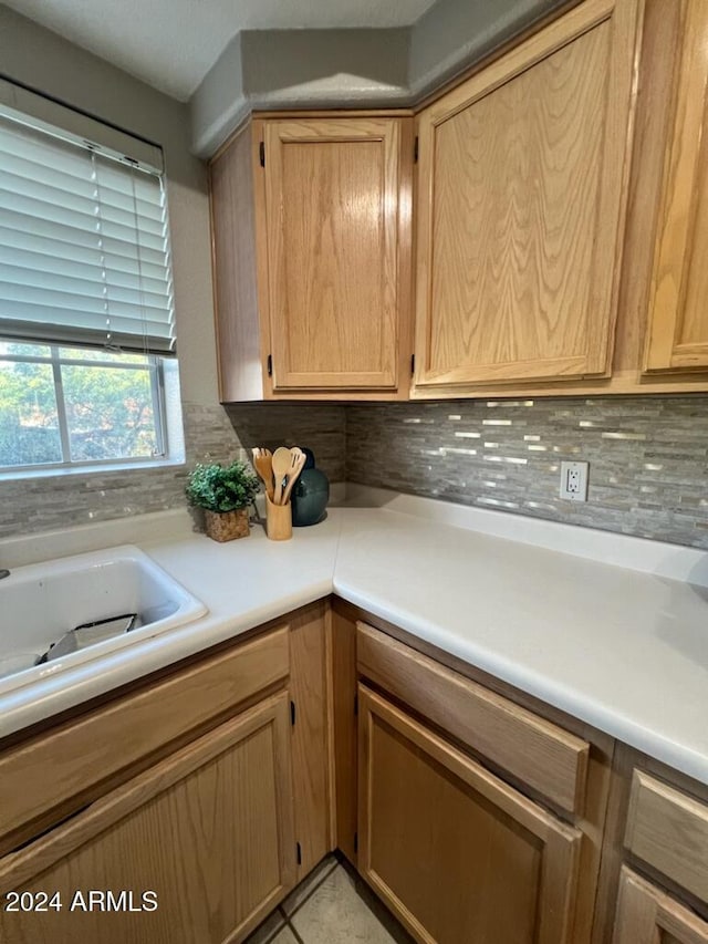 kitchen with light brown cabinetry, light tile patterned flooring, sink, and decorative backsplash