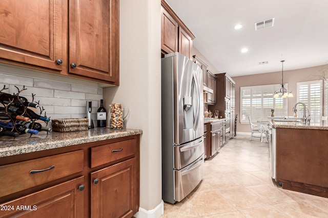 kitchen with light stone counters, hanging light fixtures, a chandelier, stainless steel fridge with ice dispenser, and backsplash