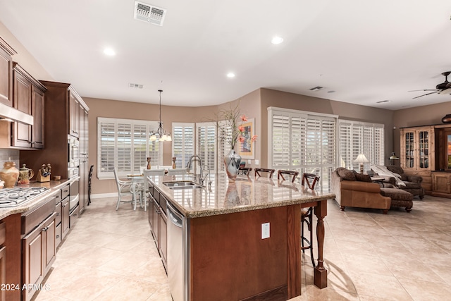 kitchen with a kitchen bar, light stone counters, hanging light fixtures, sink, and a kitchen island with sink