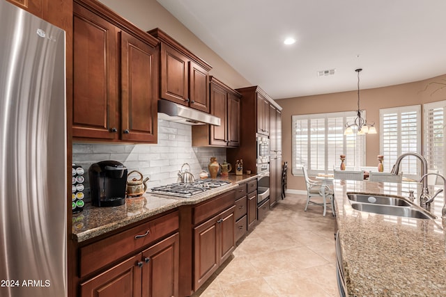 kitchen with light stone countertops, appliances with stainless steel finishes, sink, and a notable chandelier