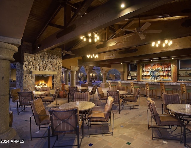 dining space featuring ceiling fan, ornate columns, beam ceiling, high vaulted ceiling, and an outdoor stone fireplace