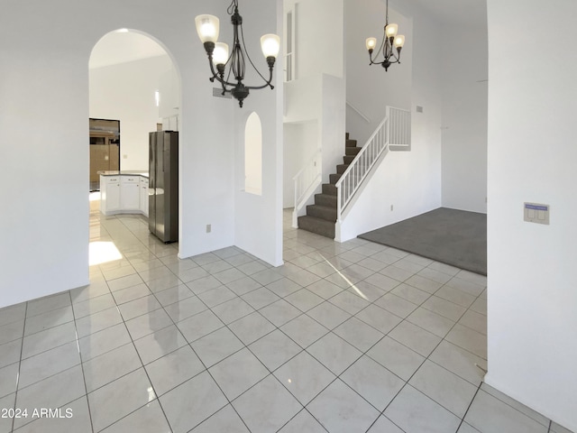 spare room featuring light tile patterned floors, a towering ceiling, and a notable chandelier