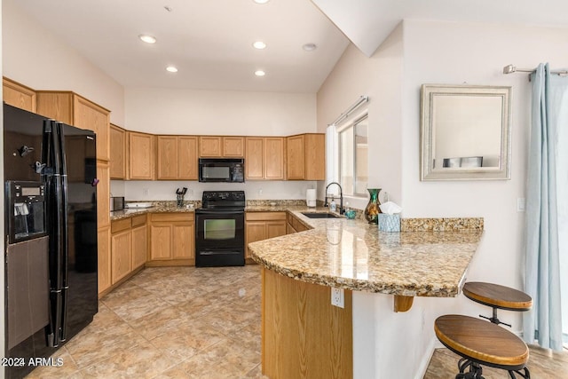 kitchen with kitchen peninsula, light stone counters, a breakfast bar, black appliances, and sink