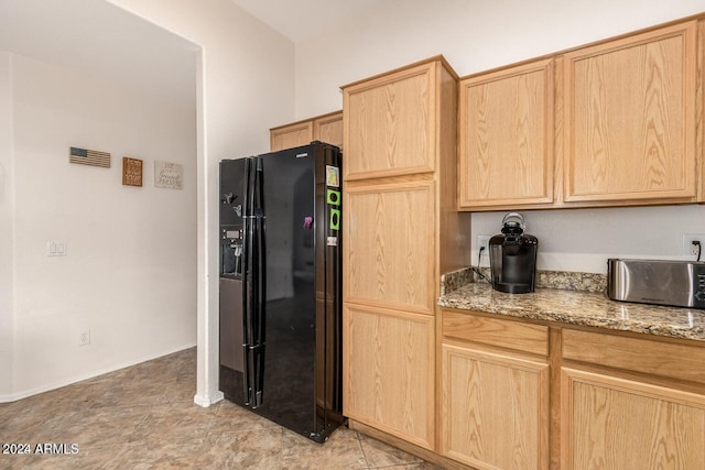 kitchen featuring light brown cabinetry, light stone countertops, light tile patterned flooring, and black fridge