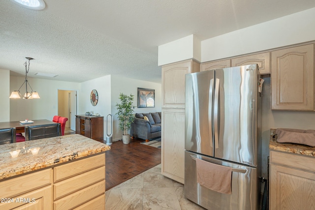 kitchen with light brown cabinets, stainless steel refrigerator, a textured ceiling, and light wood-type flooring