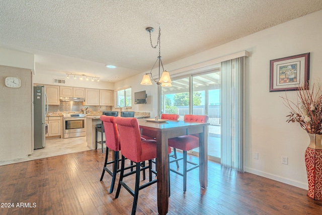 dining area with track lighting, light hardwood / wood-style flooring, a textured ceiling, and an inviting chandelier