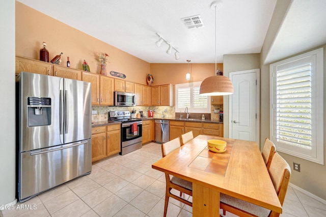 kitchen featuring appliances with stainless steel finishes, light tile patterned flooring, a sink, decorative backsplash, and dark countertops