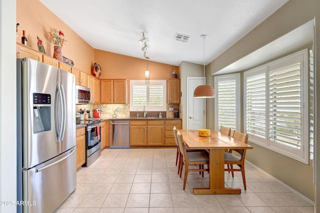 kitchen featuring stainless steel appliances, lofted ceiling, a sink, light tile patterned flooring, and backsplash
