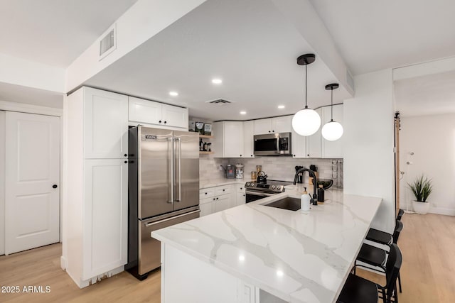 6835 E Friess Dr, Scottsdale, AZ 85254 - kitchen featuring appliances with stainless steel finishes, a peninsula, a sink, light wood-style flooring, and light stone countertops