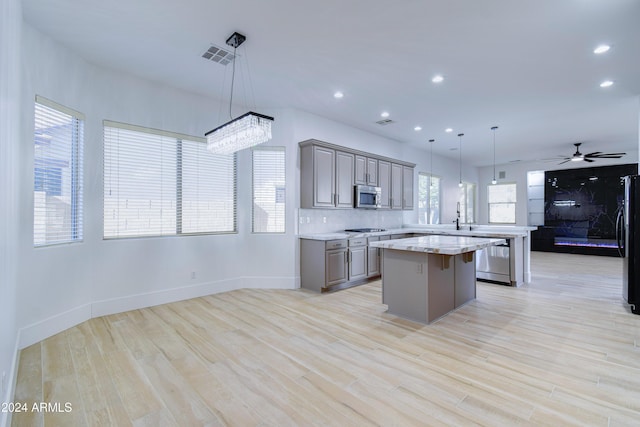 kitchen featuring a kitchen bar, ceiling fan with notable chandelier, stainless steel appliances, decorative light fixtures, and a center island