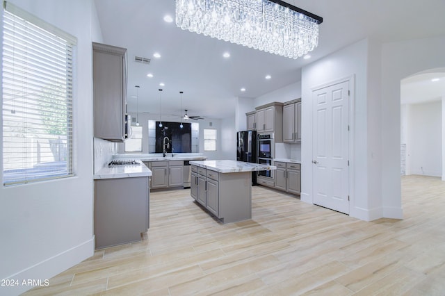 kitchen featuring ceiling fan, a center island, stainless steel appliances, decorative light fixtures, and gray cabinets