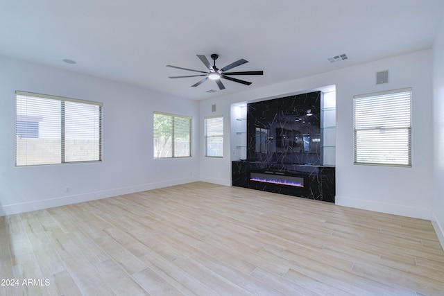 unfurnished living room featuring ceiling fan, a high end fireplace, and light wood-type flooring