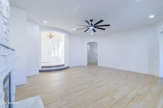 unfurnished living room featuring a stone fireplace, ceiling fan with notable chandelier, and light wood-type flooring