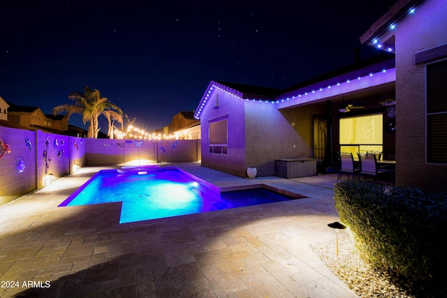 pool at night featuring a hot tub, ceiling fan, and a patio area