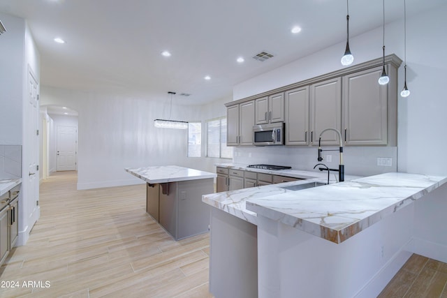 kitchen with a center island, hanging light fixtures, a breakfast bar area, gray cabinets, and stainless steel appliances