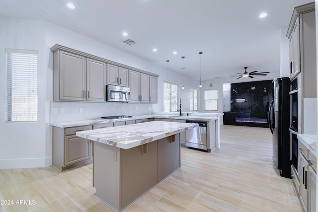 kitchen featuring a center island, hanging light fixtures, ceiling fan, light stone counters, and stainless steel appliances