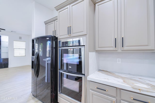 kitchen with light stone countertops, stainless steel double oven, black refrigerator with ice dispenser, light hardwood / wood-style flooring, and gray cabinets