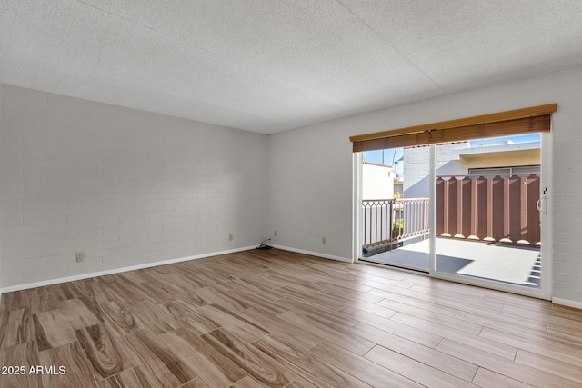 empty room featuring brick wall, a textured ceiling, and light hardwood / wood-style floors