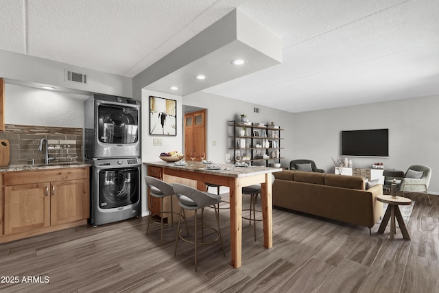 kitchen featuring stacked washer and clothes dryer, sink, dark hardwood / wood-style floors, a textured ceiling, and light stone counters