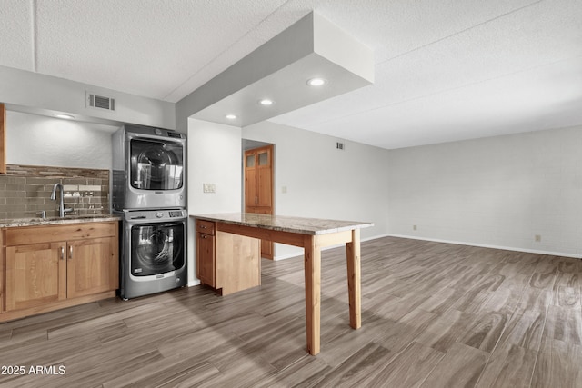 kitchen with hardwood / wood-style floors, sink, stacked washing maching and dryer, a textured ceiling, and tasteful backsplash