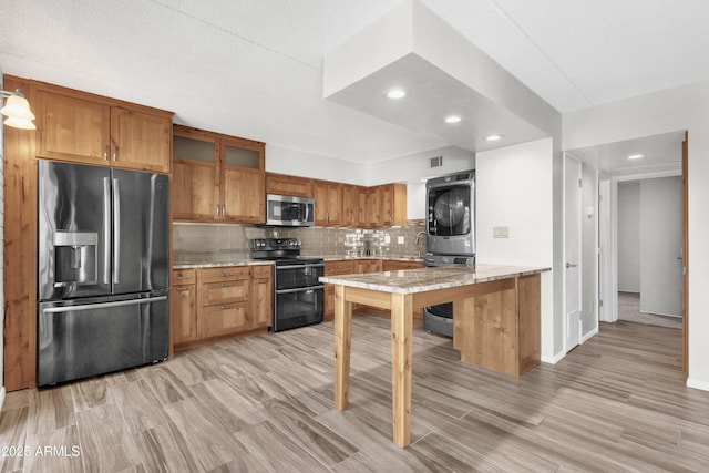 kitchen with decorative backsplash, light stone countertops, light wood-type flooring, appliances with stainless steel finishes, and stacked washer / drying machine