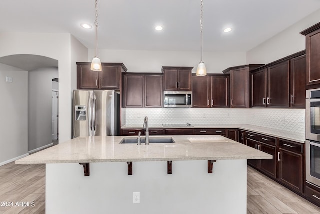 kitchen featuring sink, hanging light fixtures, light stone countertops, a kitchen bar, and stainless steel appliances