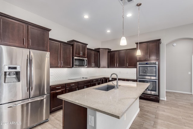 kitchen with light stone countertops, sink, an island with sink, pendant lighting, and appliances with stainless steel finishes
