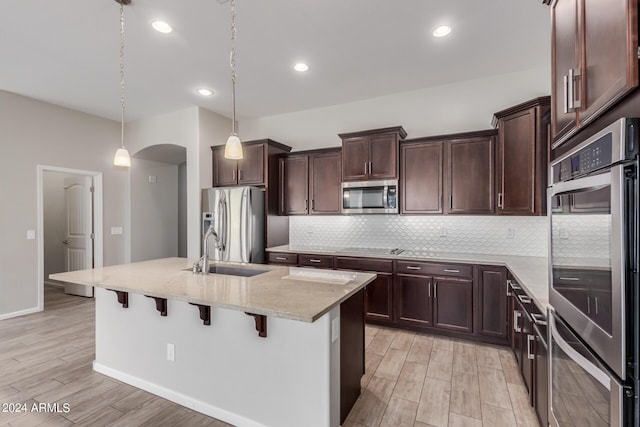 kitchen featuring stainless steel appliances, a kitchen island with sink, sink, hanging light fixtures, and a breakfast bar area