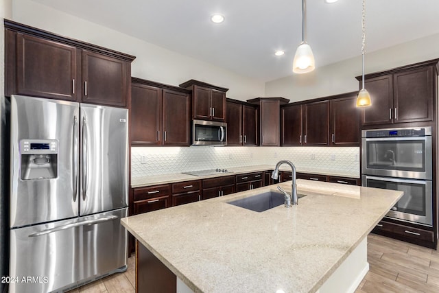 kitchen featuring an island with sink, stainless steel appliances, hanging light fixtures, and sink
