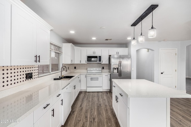 kitchen featuring arched walkways, dark wood-style flooring, stainless steel appliances, decorative backsplash, and a sink