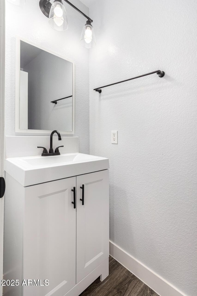 bathroom with a textured wall, baseboards, wood finished floors, and vanity