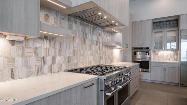 kitchen featuring gray cabinetry, wall chimney range hood, tasteful backsplash, and appliances with stainless steel finishes