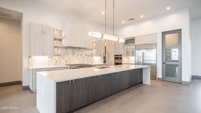 kitchen featuring sink, appliances with stainless steel finishes, a kitchen island with sink, decorative backsplash, and decorative light fixtures