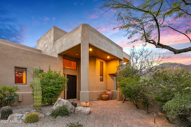 exterior entry at dusk with a mountain view and a patio