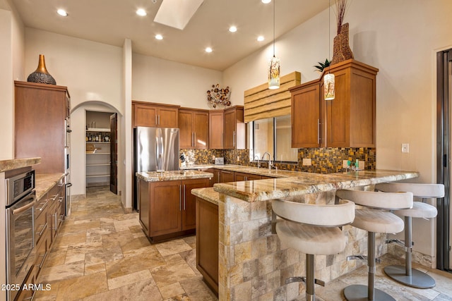 kitchen featuring a high ceiling, appliances with stainless steel finishes, a kitchen island, light stone counters, and kitchen peninsula