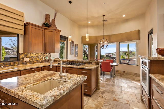 kitchen with sink, a chandelier, a high ceiling, hanging light fixtures, and an island with sink