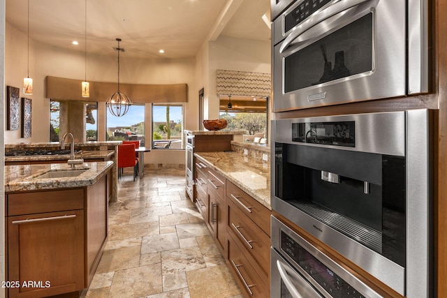 kitchen featuring light stone countertops, backsplash, sink, pendant lighting, and an inviting chandelier