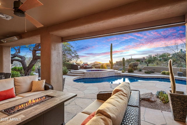 pool at dusk featuring a patio area, an in ground hot tub, ceiling fan, and an outdoor living space with a fire pit