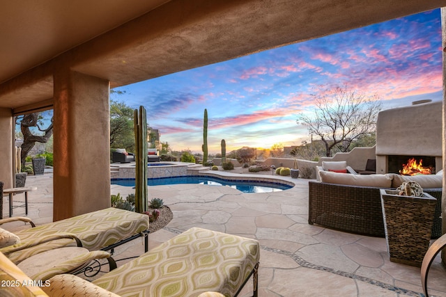 pool at dusk with an outdoor living space with a fireplace, an in ground hot tub, and a patio