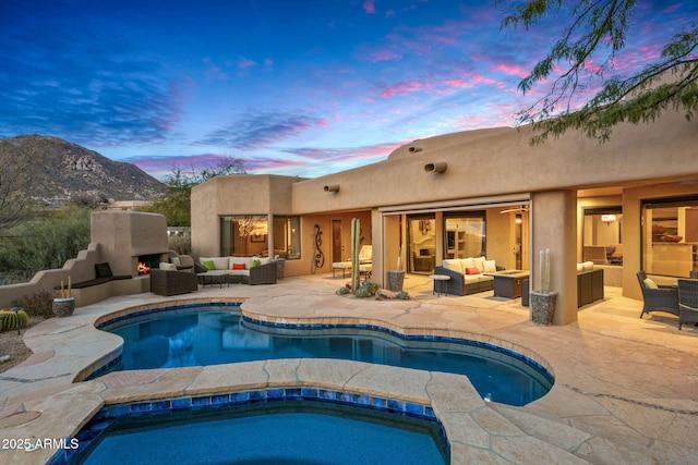 pool at dusk with an outdoor living space with a fireplace, a mountain view, and a patio area