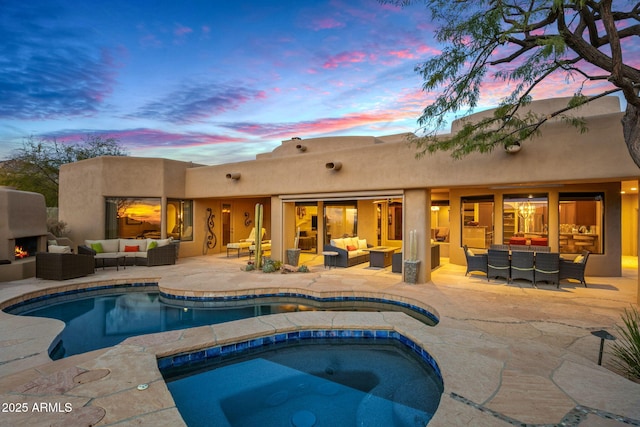 pool at dusk with an outdoor living space with a fireplace, an in ground hot tub, and a patio