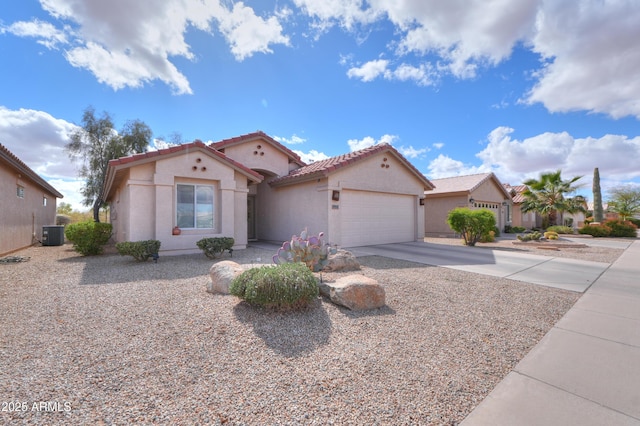 mediterranean / spanish house with an attached garage, central air condition unit, a tile roof, concrete driveway, and stucco siding