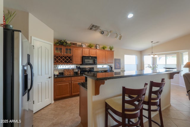 kitchen with brown cabinets, light tile patterned floors, visible vents, black appliances, and a kitchen breakfast bar