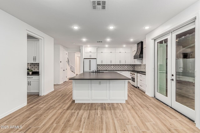 20412 W Thayer St, Buckeye, AZ 85396 - kitchen featuring premium appliances, dark countertops, light wood-style flooring, custom exhaust hood, and backsplash