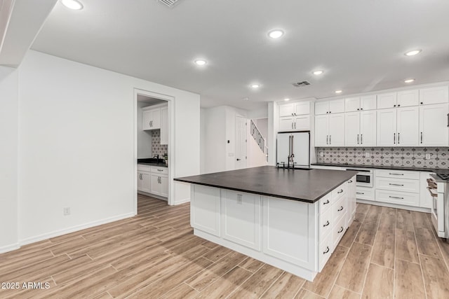 20412 W Thayer St, Buckeye, AZ 85396 - kitchen featuring white fridge, dark countertops, light wood-style flooring, tasteful backsplash, and white cabinets