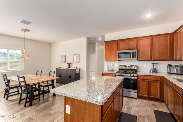 kitchen with appliances with stainless steel finishes, light hardwood / wood-style flooring, hanging light fixtures, and a kitchen island