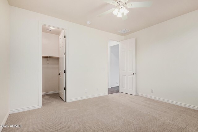 unfurnished bedroom featuring carpet floors, a spacious closet, baseboards, and a ceiling fan