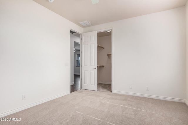 unfurnished bedroom with a walk in closet, carpet flooring, visible vents, and baseboards